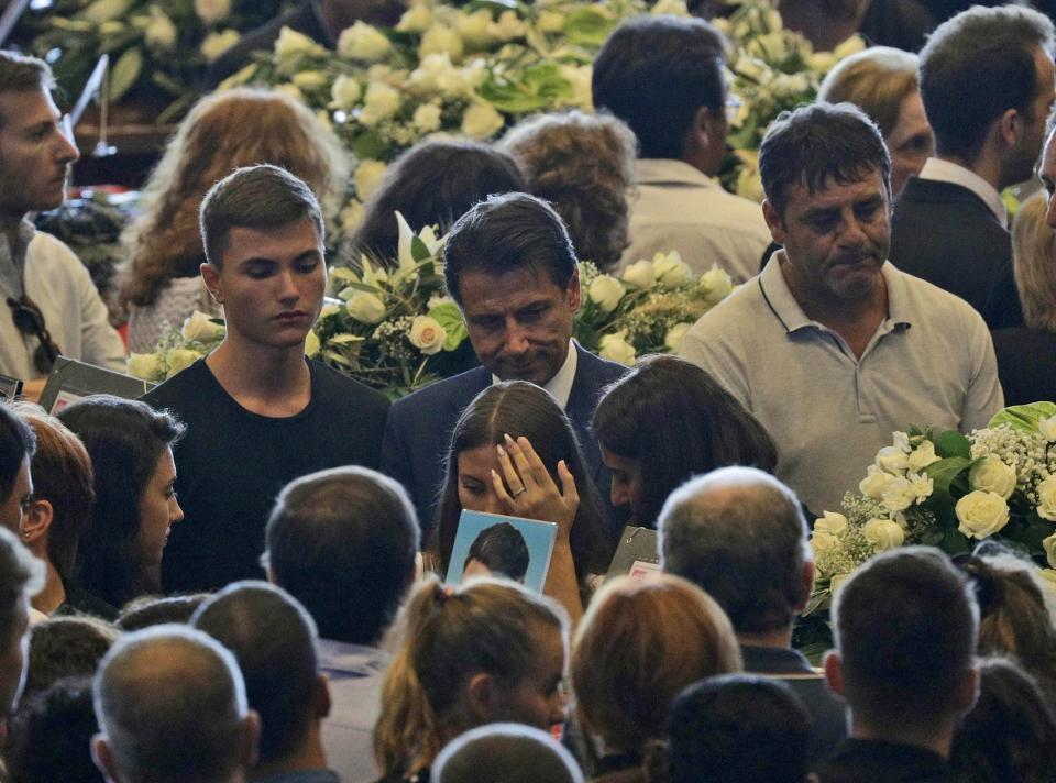 Italian Premier Giuseppe Conte, center, walks past relatives of some of the victims of a collapsed highway bridge at the end of their funeral service, in Genoa's exhibition center Fiera di Genova, Italy, Saturday, Aug. 18, 2018. Saturday has been declared a national day of mourning in Italy and includes a state funeral at the industrial port city's fair grounds for those who plunged to their deaths as the 45-meter (150-foot) tall Morandi Bridge gave way Tuesday. (AP Photo/Gregorio Borgia)