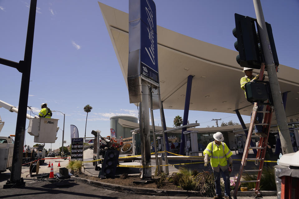 Los Angeles City Public Works technicians replace burned traffic lights and signs after crash involving multiple cars near a gas station in the unincorporated Windsor Hills in Los Angeles on Friday, Aug. 5, 2022. A speeding car ran a red light and plowed into cars in a crowded intersection Thursday in a fiery crash that killed several people, including a baby, just outside of Los Angeles, authorities said. (AP Photo/Damian Dovarganes)