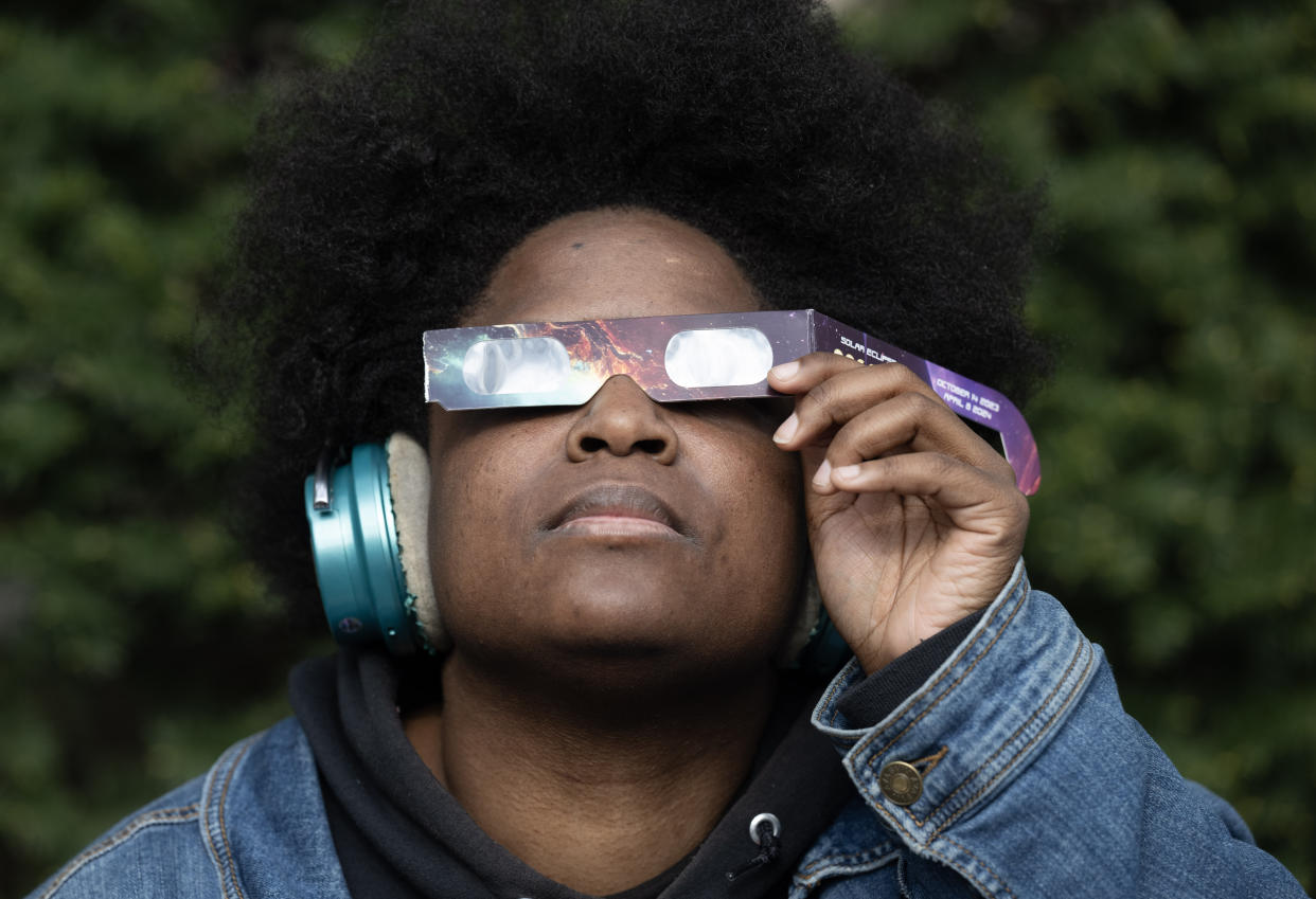 A man holding eclipse glasses in front of his eyes and looking up.