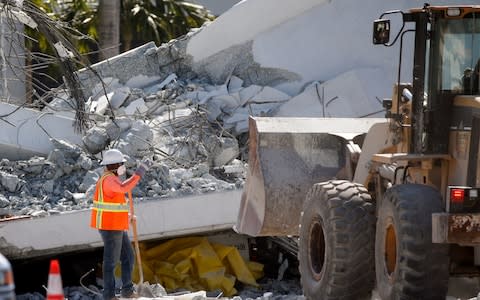 Workers use a front loader to clear debris from a section of a collapsed pedestrian bridge - Credit: AP