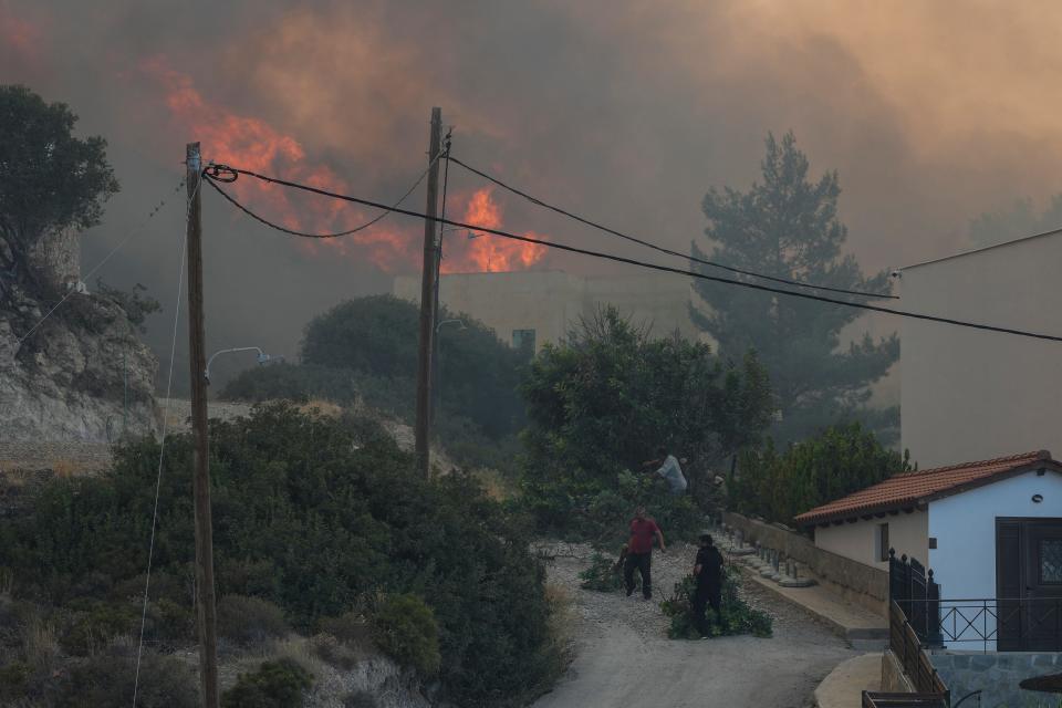 Locals pull branches from a forest fire in the village of Gennadi on the Aegean island of Rhodes, southeastern Greece, Tuesday, July 25, 2023. A firefighting plane has crashed in southern Greece, killing both crew members, as authorities battle fires across the country as heatwave temperatures return. (AP Photo/Petros Giannakouris)