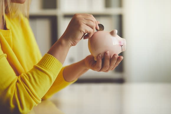 Woman putting a coin into a piggy bank.