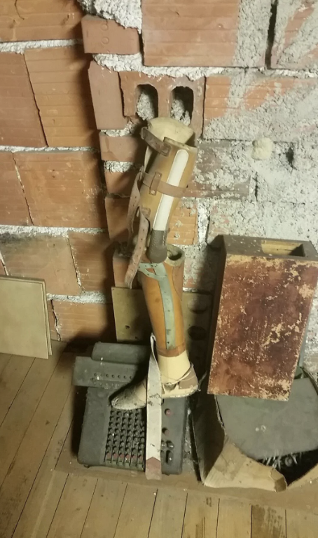Vintage wooden mannequin with articulated joints standing among old metal objects against a brick wall