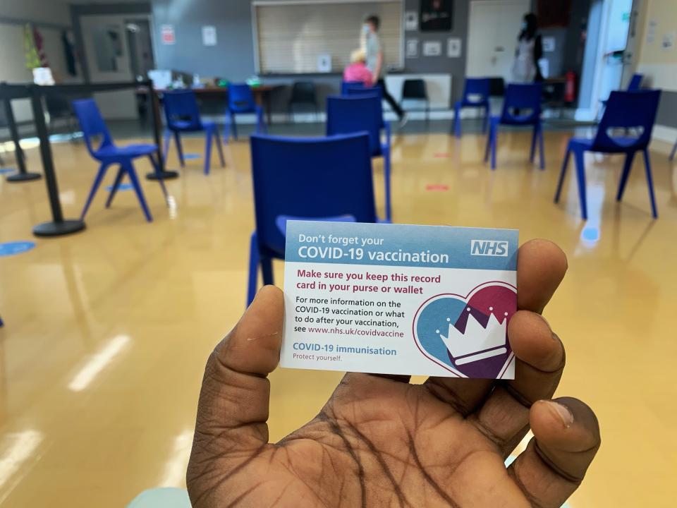 A hand holds up a vaccination card with empty chairs in the background.