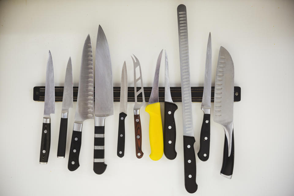 Various kitchen knives are displayed on a magnetic strip, showcasing different blade shapes and handle designs