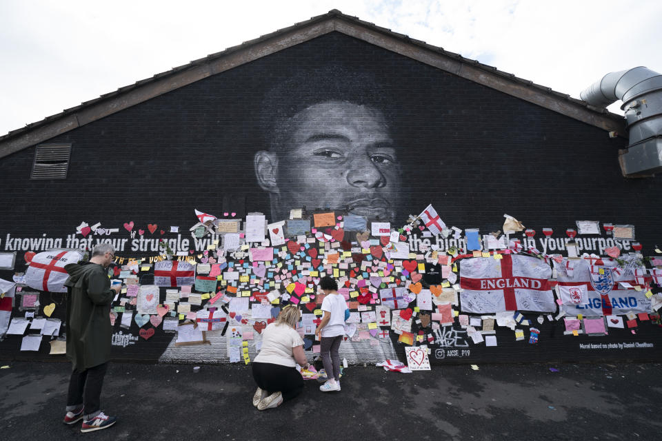 People look at the messages of support left on a mural of Manchester United striker and England player Marcus Rashford, on the wall of the Coffee House Cafe on Copson Street, in Withington, Manchester, England, Tuesday July 13, 2021. The mural was defaced with graffiti in the wake of England losing the Euro 2020 soccer championship final match to Italy. (AP Photo/Jon Super)