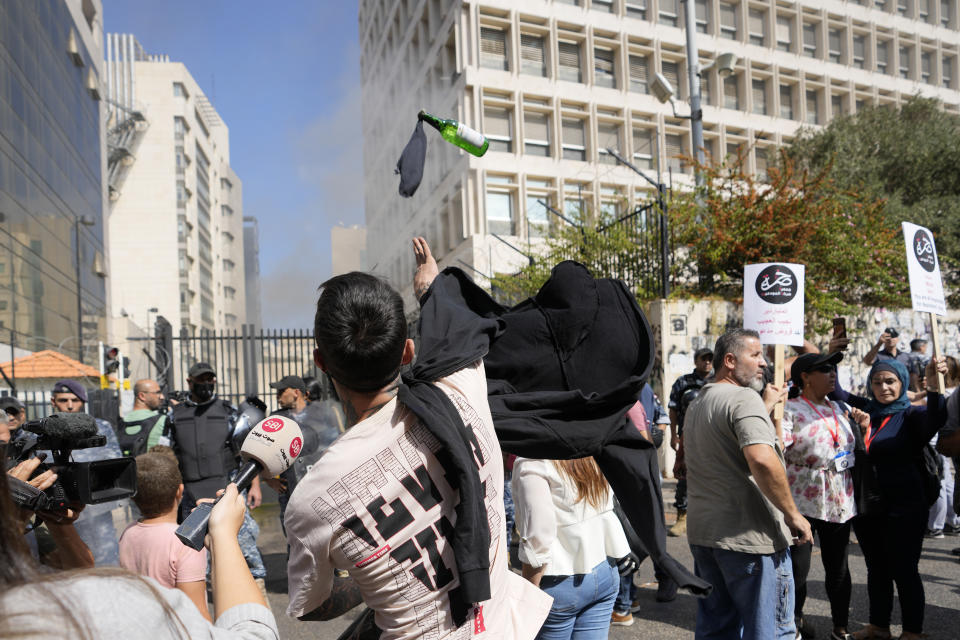A protester throws a molotov cocktail at the Lebanese Central Bank building, background, where the anti-government demonstrators rally against the Lebanese Central Bank Governor Riad Salameh and the deepening financial crisis, in Beirut, Lebanon, Wednesday, Oct. 5, 2022. (AP Photo/Hassan Ammar)