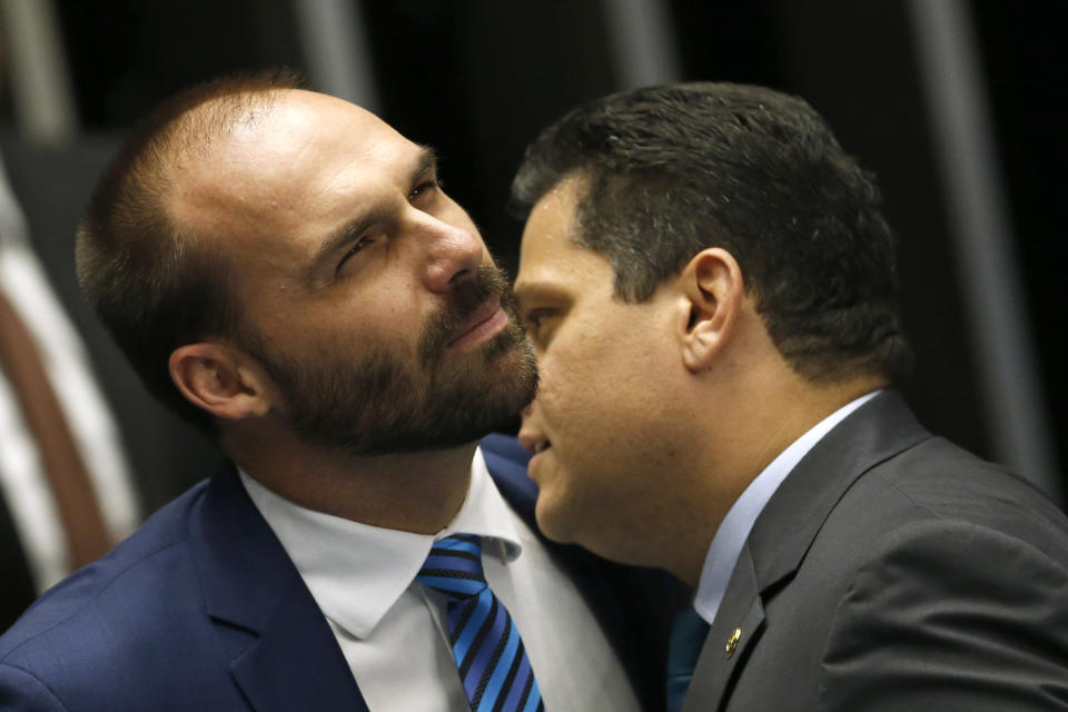 Brazil's Senate President Davi Alcolumbre, right, speaks into the ear of lawmaker Eduardo Bolsonaro, son of the nation's president, during the final voting session on pension reform at the Senate in Brasilia, Brazil, Tuesday, Oct. 22, 2019. The most meaningful impact of the reform is the establishment of a minimum age for retirement at 65 for men and 62 for women. (AP Photo/Eraldo Peres)