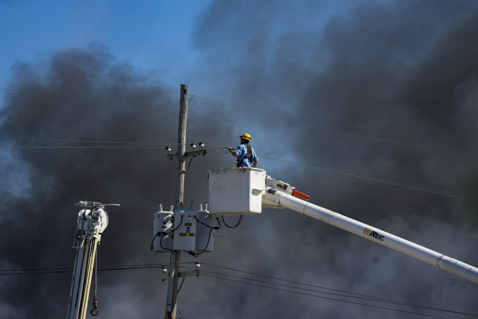 Utility workers remove utilities from the area as smoke billows from an industrial fire in Richmond, Ind., Wednesday, April 12, 2023. Authorities urged people to evacuate if they live near the fire. The former factory site was used to store plastics and other materials for recycling or resale. (AP Photo/Michael Conroy)