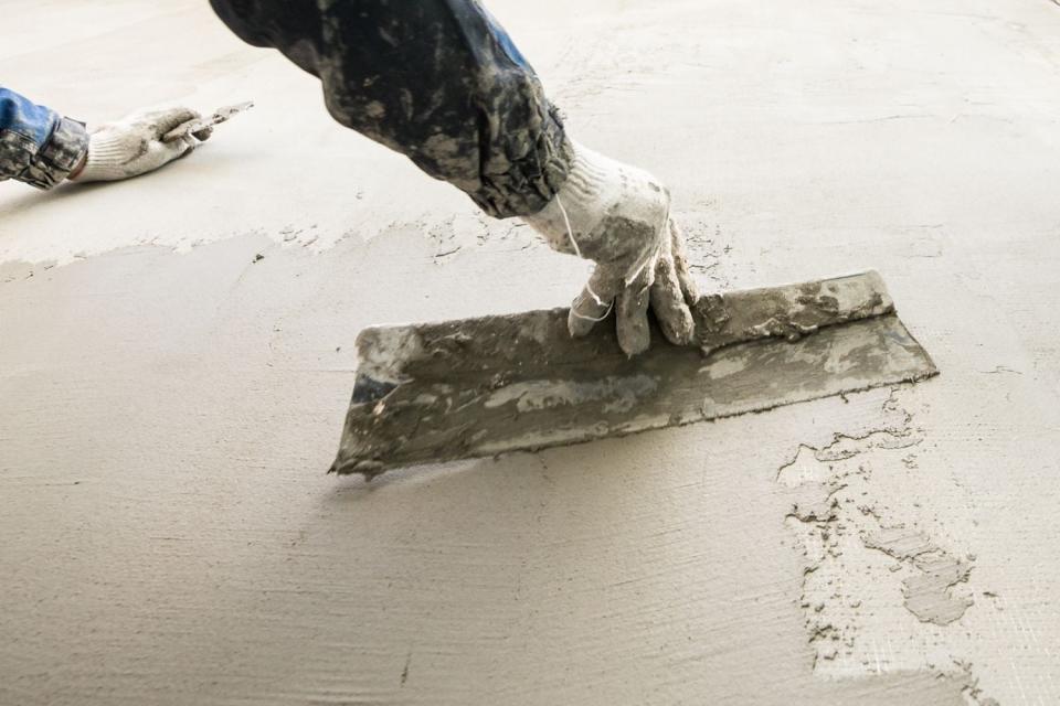 A close up of a gloved hand leveling concrete. 