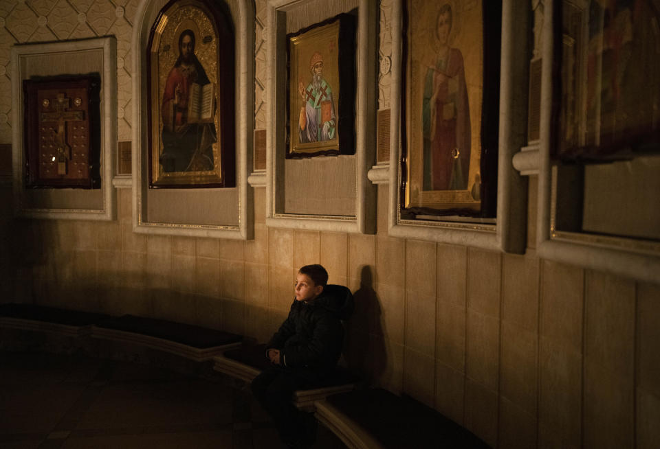 A child sits on a bench during a religious service inside the Transfiguration of Jesus Orthodox Cathedral during blackout caused by recent Russian rocket attacks, in Kyiv, Ukraine, Saturday, Dec. 3, 2022. A top Orthodox priest in Ukraine's capital says he supports the efforts of President Volodymyr Zelenskyy's government and counter-intelligence agency to end Russian spying and meddling in Ukrainian politics through a Moscow-affiliated church. (AP Photo/Efrem Lukatsky)