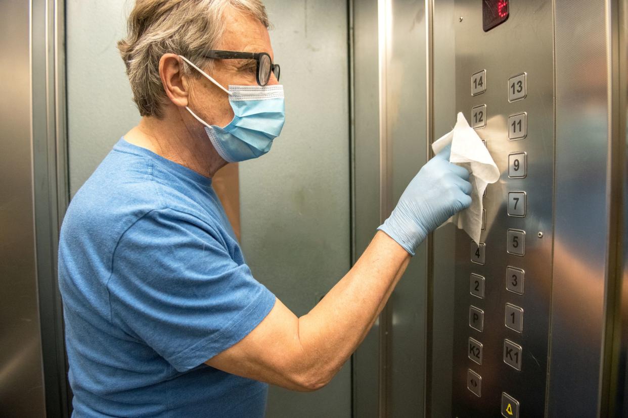 Senior man wiping down the elevator buttons