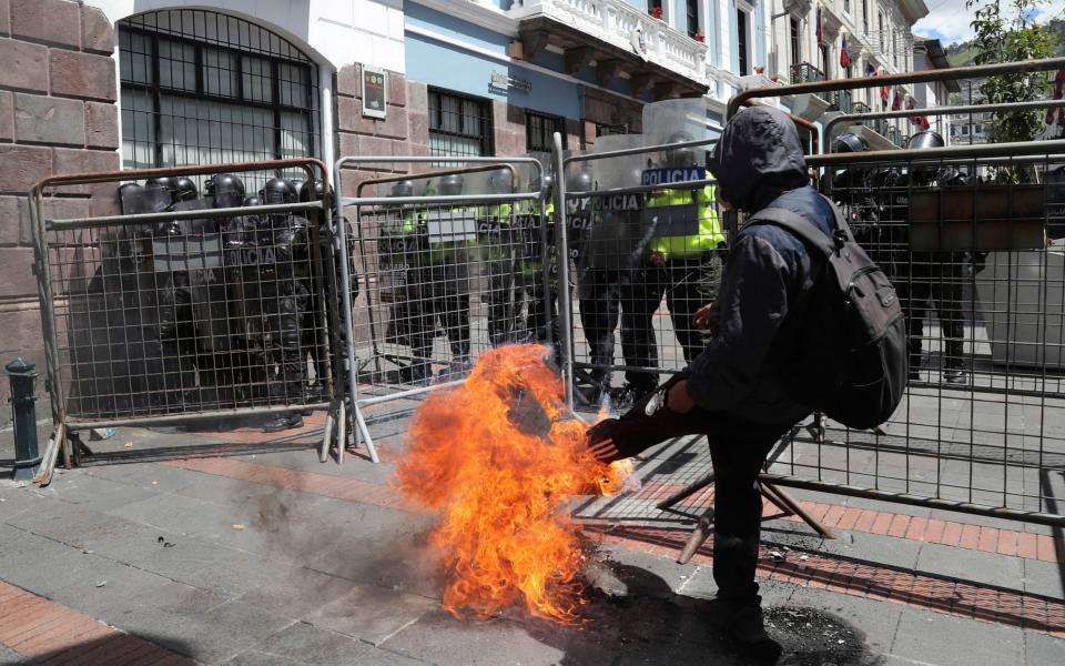 A protester kicks a burning tyre at a police barricade in Quito - AP