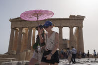 Tourists with an umbrella walk in front of the Parthenon at the ancient Acropolis in central Athens, Wednesday, June 12, 2024. The ancient site was closed to the public for five hours due to a heat wave that pushed temperatures to 39 degrees Celsius (102 Fahrenheit) in the capital and even higher in parts of central Greece. (AP Photo/Petros Giannakouris)