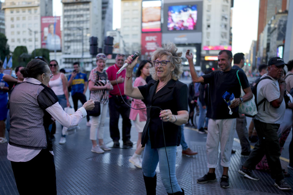 Pedestrians watch as Ámbar Imoberdoff belts out a tune on a street corner in downtown Buenos Aires, Argentina, Thursday, March 7, 2024. Thanks to her impromptu recitals, Imoberdoff, who is a widow and has no children, says she can earn up to $200 on a good night during the weekends. “God has given me a spirit of not giving in to things. Death is going to find me standing and singing,” she said. (AP Photo/Natacha Pisarenko)