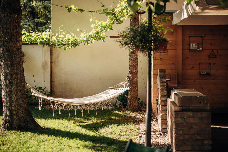 A rope hammock hung between two trees in a backyard