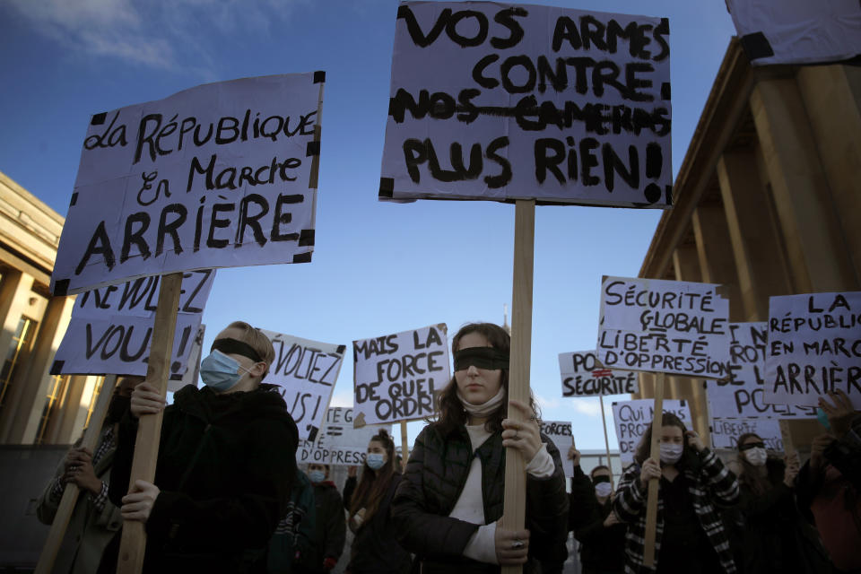 Demonstrators chant slogans during a protest against bill on police images, in Paris, Saturday, Nov. 21, 2020. Thousands of people took to the streets in Paris and other French cities Saturday to protest a proposed security law they say would impinge on freedom of information and media rights. The board reads: Your guns against our cameras. (AP Photo/Christophe Ena)