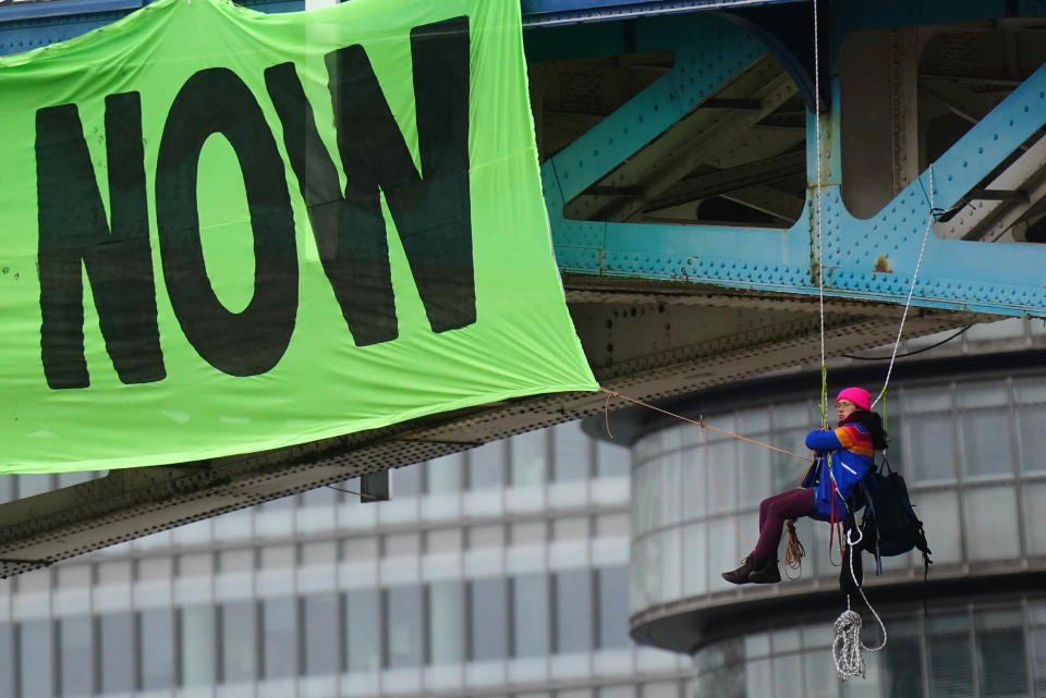 Activists from Extinction Rebellion hang from suspension cords beside a giant banner that reads 