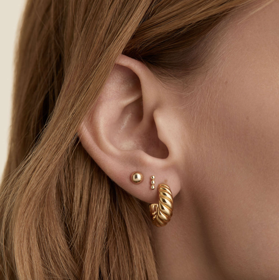 woman wearing gold stud earring and gold Croissant Dôme Hoops (Photo via Mejuri)