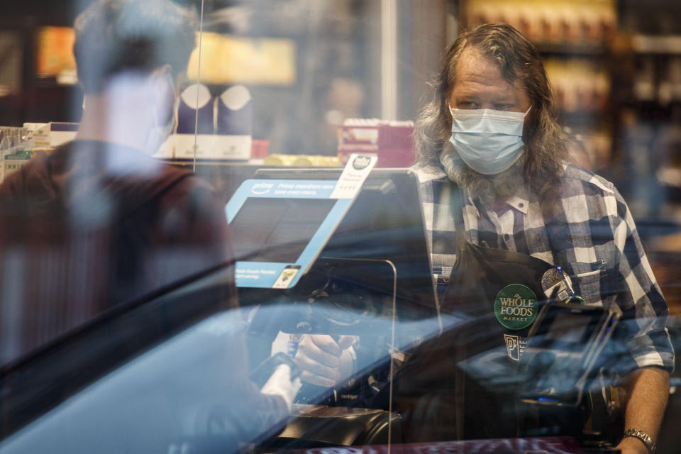 Un empleado de Whole Foods Market con cubrebocas durante la pandemia de coronavirus, frente a una caja registradora, en Washington, el 14 de abril de 2020. (Ting Shen/The New York Times)