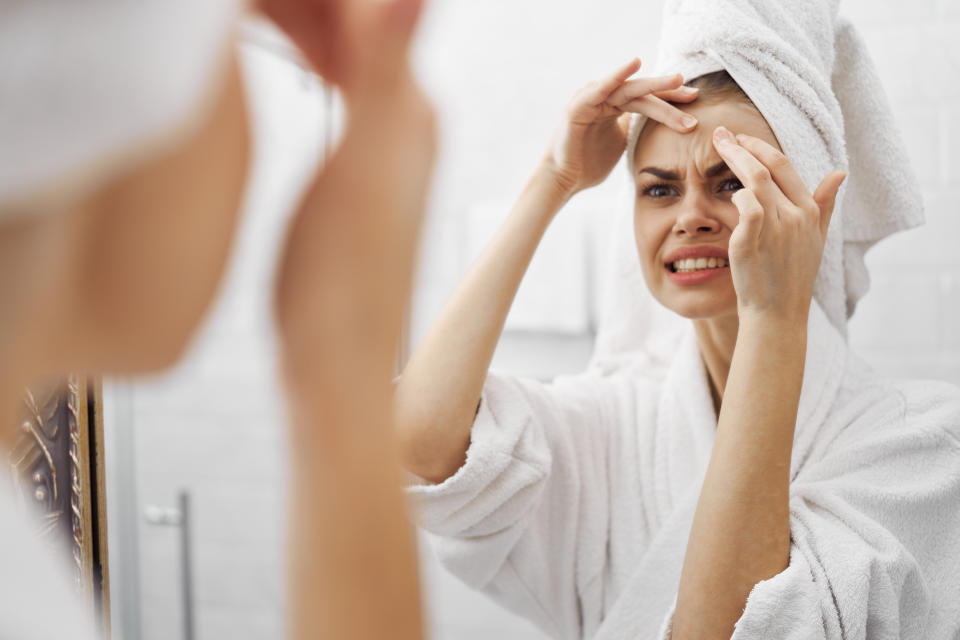 Person in bathrobe examines their forehead in the mirror, looking concerned