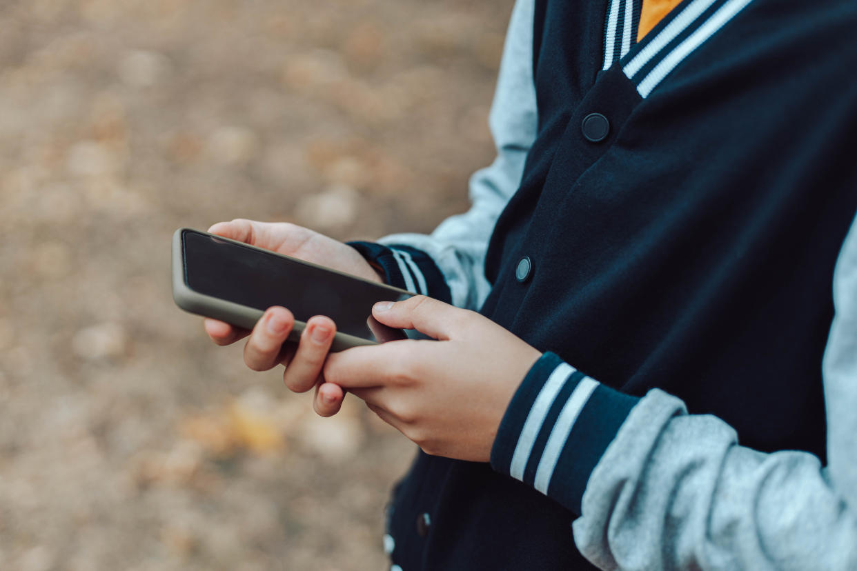 Child hands uses smartphone in summer park, looking at screen of devices