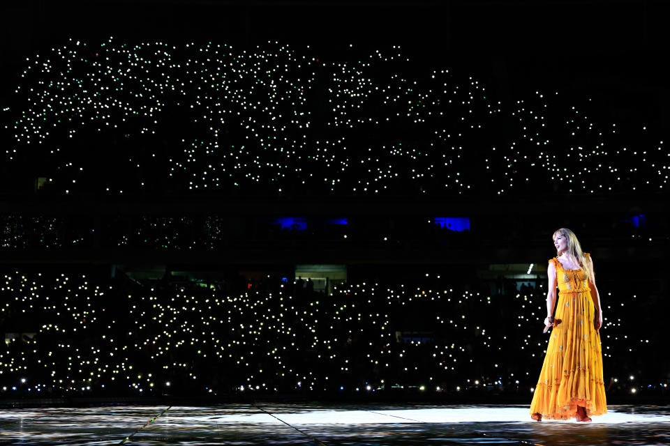 Taylor Swift onstage with lights from the crowd behind her