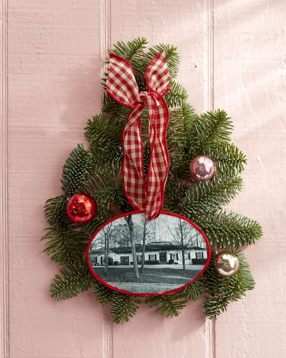 a home photo made into an ornament with greenery and small christmas balls surrounding it