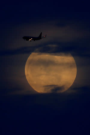 A full moon rises between clouds as a landing commercial jet approaches the airport before the start of a total lunar eclipse that is being called a 'Super Blood Wolf Moon' in San Diego, California, U.S., January 20, 2019. REUTERS/Mike Blake