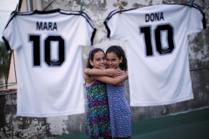 Mara y Dona, hijas mellizas de Walter Gastón Rotundo, un fanático de Diego Maradona que nombró a sus hijas en honor al astro del fútbol, se abrazan mientras posan cerca de camisetas de la selección argentina con sus nombres, en Buenos Aires