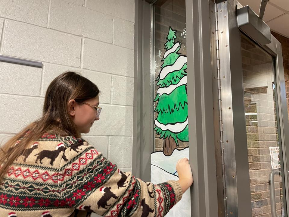 Port Huron Northern junior Addy Neilsen paints a snowcapped tree on one of the windows at Keewahdin Elementary School on Nov. 21, 2023.