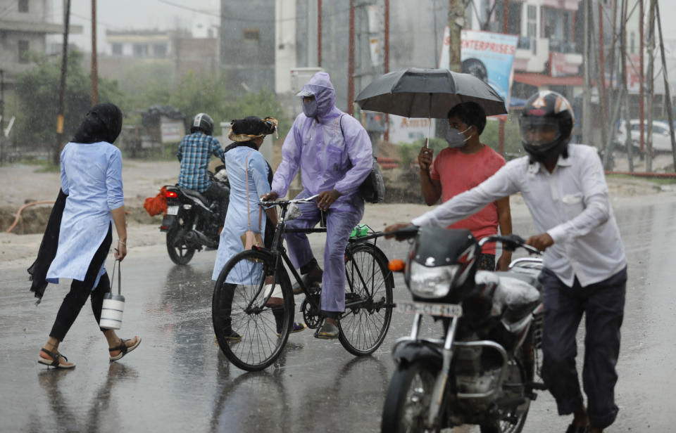 People wear face masks and move through a street in the rain in Prayagraj, India, Wednesday, July 29, 2020. India is the third hardest-hit country by the pandemic in the world after the United States and Brazil. (AP Photo/Rajesh Kumar Singh)