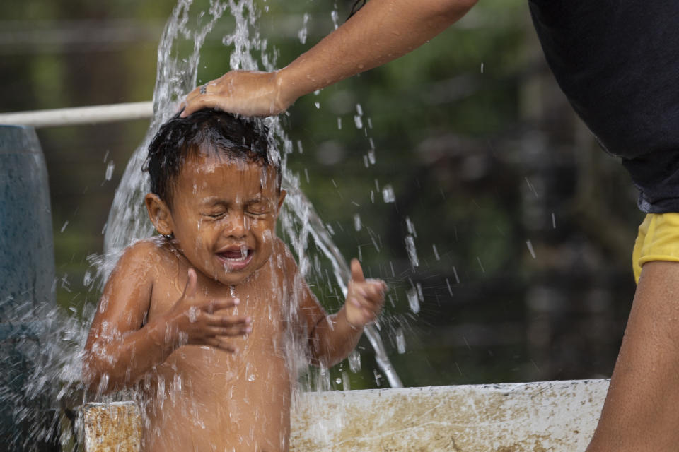 A mother bathes her child at a shelter for those like them who lost their homes during last year's hurricanes Eta and Iota in La Lima, on the outskirts of San Pedro Sula, Honduras, Monday, Jan. 11, 2021. The World Food Program says the number of Hondurans facing food insecurity is 3 million, six times higher than before. (AP Photo/Moises Castillo)