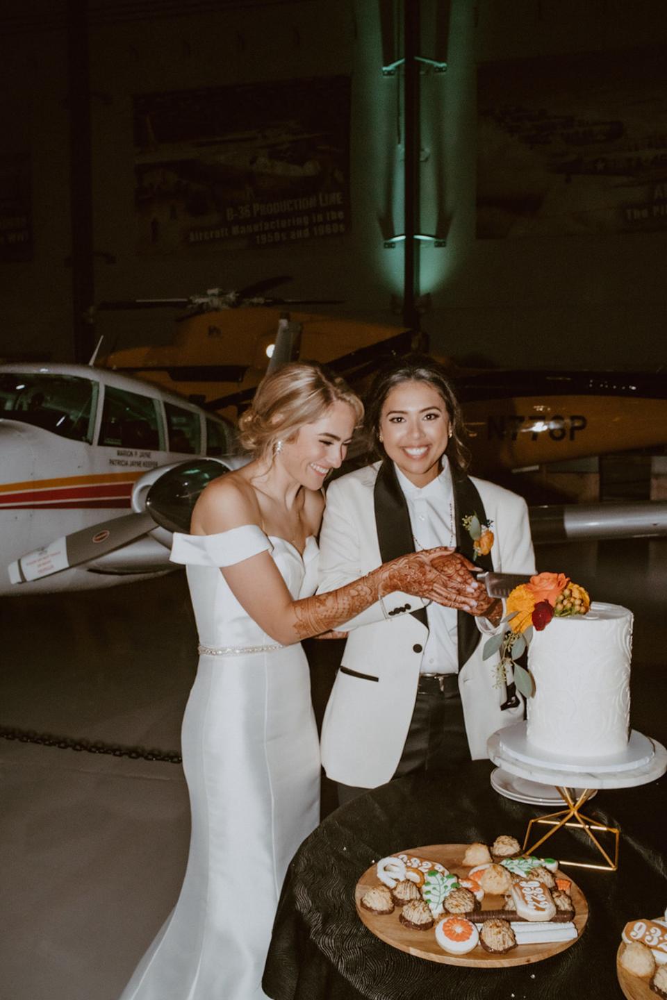 TWo brides cut their wedding cake in front of a plane.