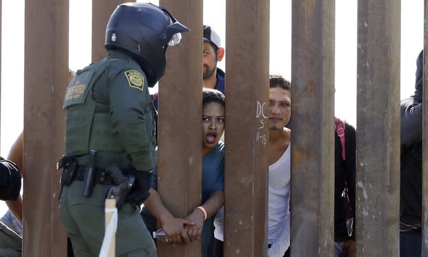 Migrants from Central America talking to a U.S. Border Patrol Agent through a border wall in San Diego.
