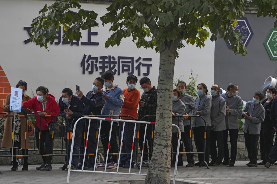 Service sector workers wearing face masks to help curb the spread of the coronavirus line up for COVID-19 test during a mass testing at a site baring the words "You and me on the road of civilization" in Beijing, Friday, Oct. 29, 2021, following a spike of the coronavirus in the capital and other provincials. (AP Photo/Andy Wong)