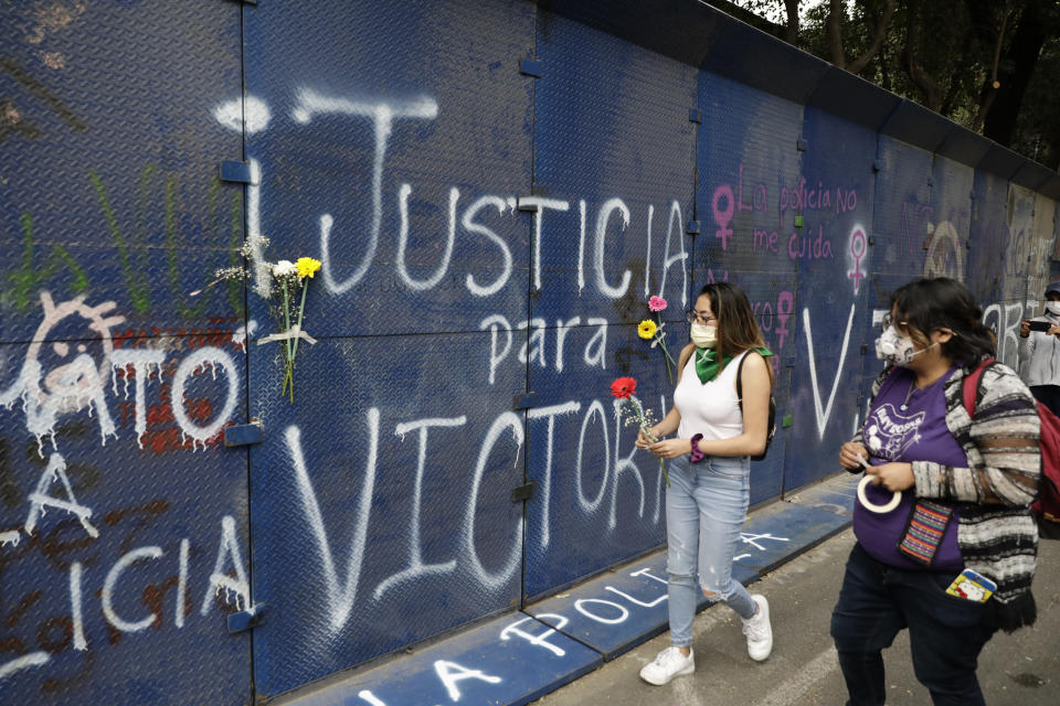 Young women bring flowers to the perimeter wall of the Quintana Roo state offices sprayed with graffiti that reads in Spanish "Justice for Victoria," during a protest in Mexico City, Monday, March. 29, 2021. The demonstrators were protesting the police killing in Tulum, Quintana Roo state, of Salvadoran national Victoria Esperanza Salazar when a female police officer knelt on her back to cuff her. Mexican authorities say an autopsy confirmed that police broke her neck. (AP Photo/Eduardo Verdugo)