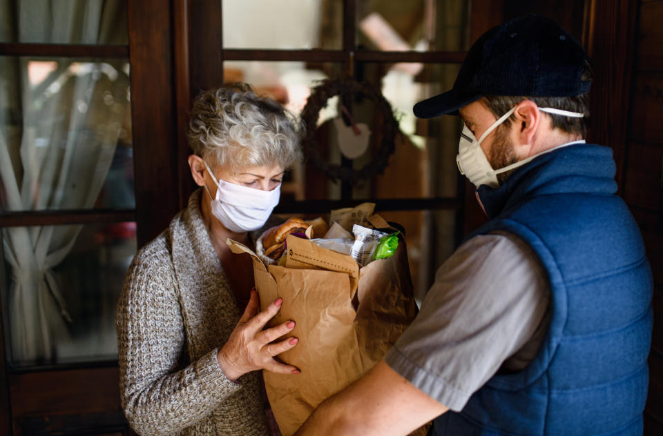 Man courier delivering shopping to senior woman with face mask, corona virus and quarantine concept.