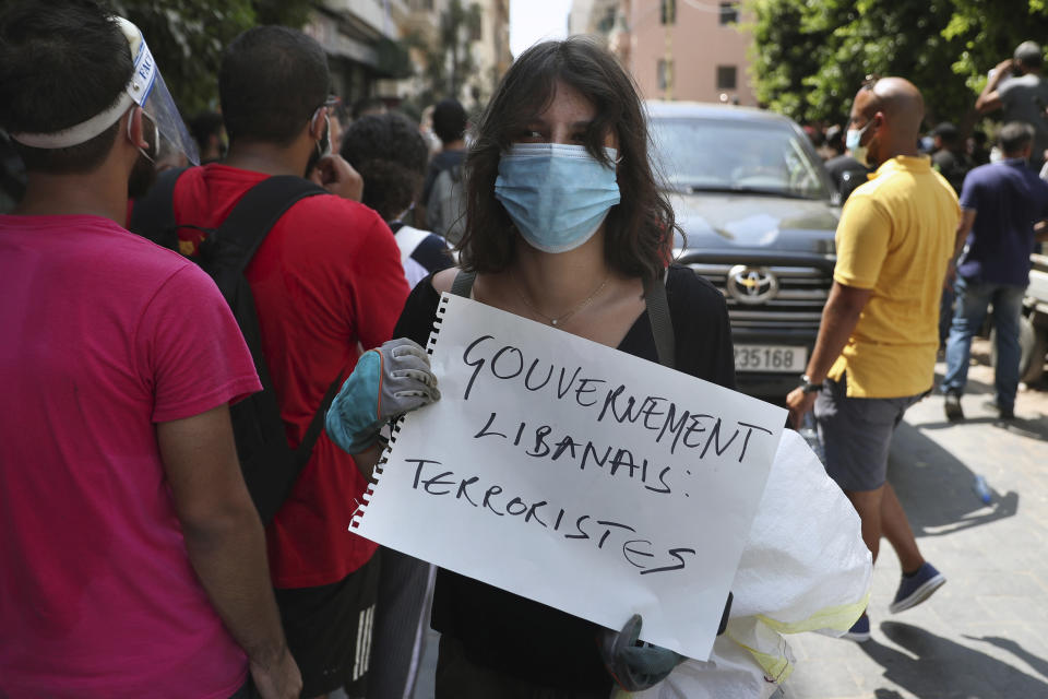 A woman holds a placard in French that reads, "Lebanese government terrorists," next to a convoy of French President Emmanuel Macron as he visits the Gemayzeh neighborhood, which suffered extensive damage from an explosion on Tuesday that hit the seaport of Beirut, Lebanon, Thursday, Aug. 6, 2020. (AP Photo/Bilal Hussein)