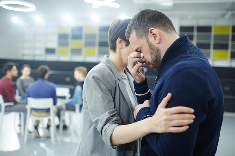 A woman with her hand on the arm of a man who seems distressed