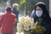 An elderly flower vendor wears a face mask for protection against COVID-19 infection in Bucharest, Tuesday, Oct. 20, 2020. Local authorities imposed the use of face masks in all public spaces, indoors and outdoors, closed schools, restaurants, theatres and cinemas after the rate of COVID-19 infections went above 3 cases per 1000 inhabitants in the Romanian capital Bucharest. (AP Photo/Andreea Alexandru)