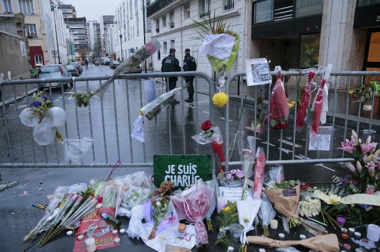 French police stand guard near floral tributes outside the Charlie Hebdo offices in Paris, on January 9, 2015