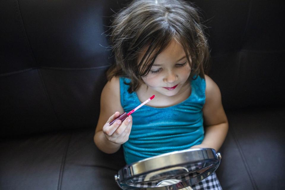 A girl holding a lipstick wand and a mirror