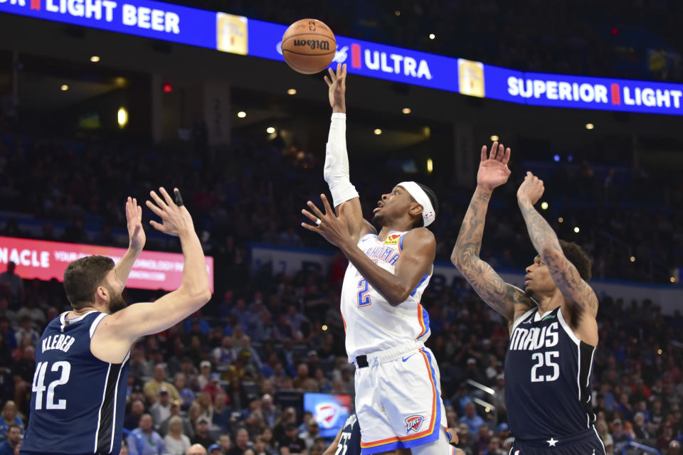 Oklahoma City Thunder guard Shai Gilgeous-Alexander (2) shoots from between Dallas Mavericks forwards Maxi Kleber (42) and P.J. Washington (25) during the second half of an NBA basketball game Thursday, March 14, 2024, in Oklahoma City. (AP Photo/Kyle Phillips)