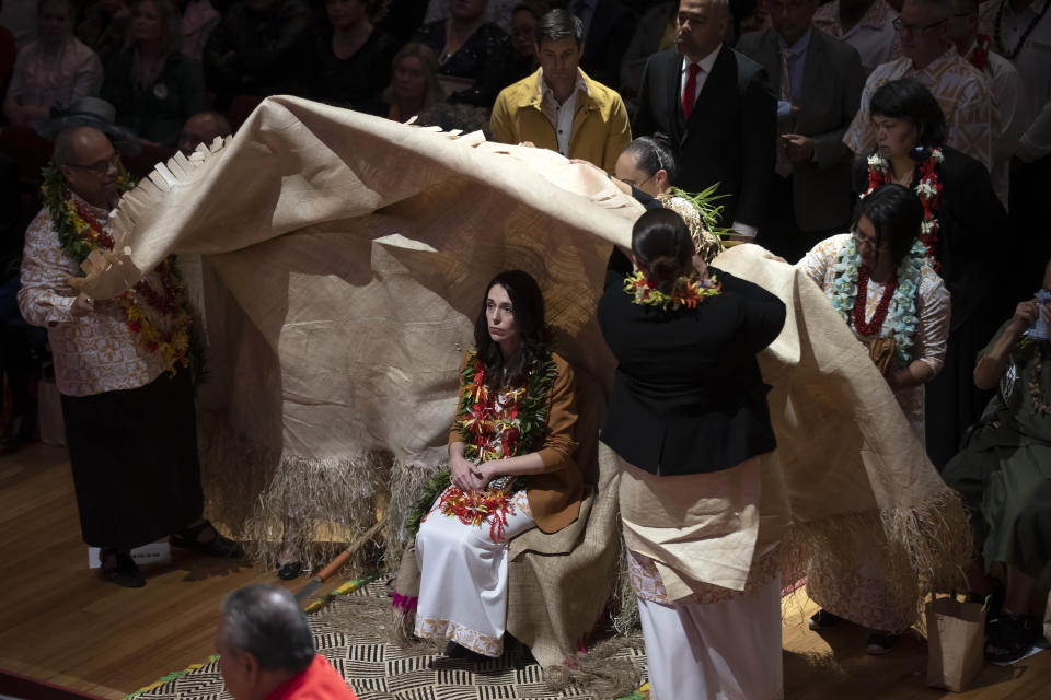 New Zealand Prime Minister Jacinda Ardern, center, is covered during a ceremony in Auckland, Sunday, Aug. 1, 2021, to formally apologize for a racially charged part of the nation's history known as the Dawn Raids. The Dawn Raids are known as the time when the Pasifika people were targeted for deportation in the mid-1970s during aggressive home raids by authorities to find, convict and deport visa overstayers. (Brett Phibbs/New Zealand Herald via AP)