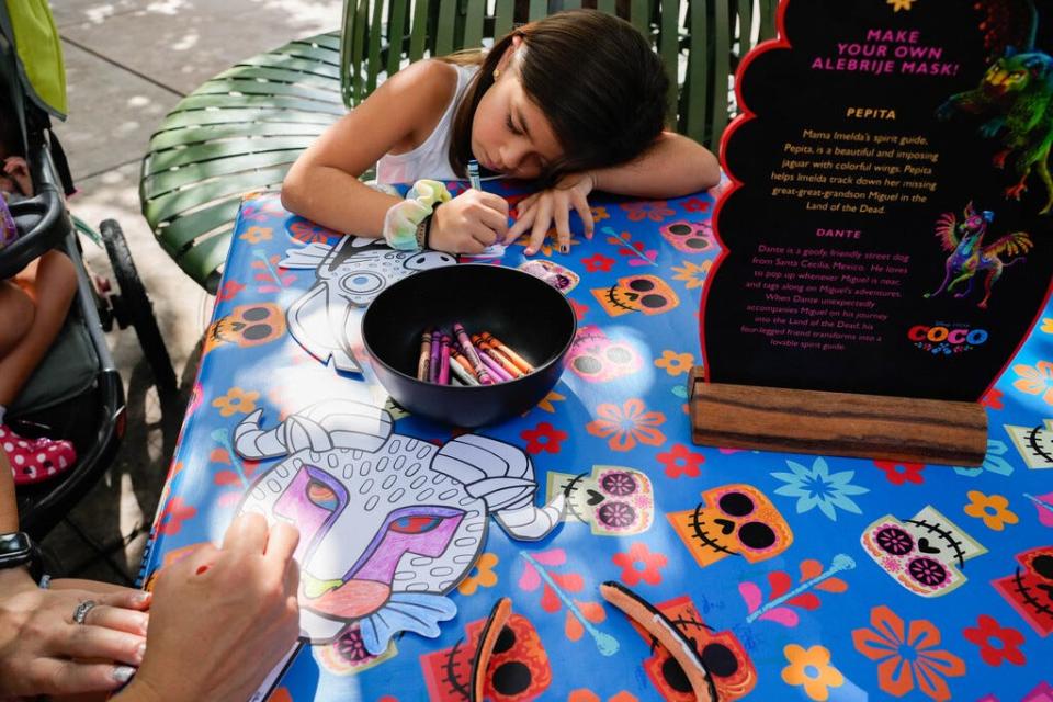 Malia Walias, 8, colors in a paper “alebrije” (Mexican folk art of fantastical creatures) mask with her mom, Rachelle Walias, 42, at Plaza de la Familia in Disney California Adventure Park.