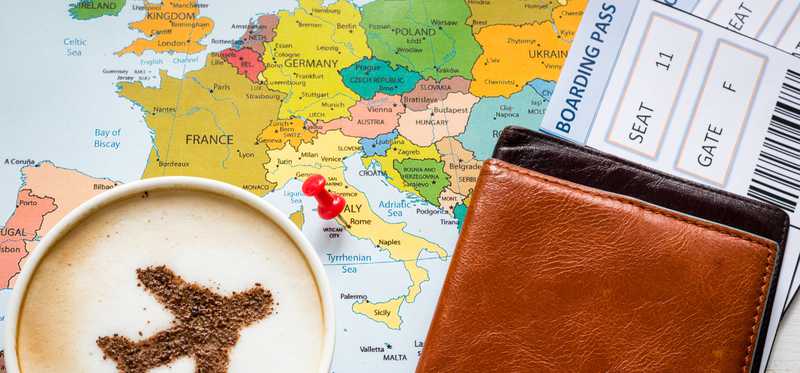 A map with a pin in it on Italy, covered by a boarding pass and a cup of coffee