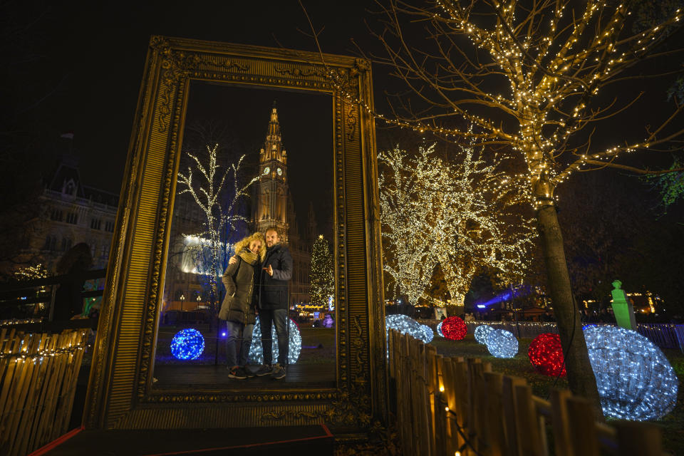 A couple poses for a photograph backdropped by the building of the city hall at a Christmas market in Vienna, Austria, Sunday, Nov. 21, 2021. The Austrian government announced a nationwide lockdown that will start Monday and comes as average daily deaths have tripled in recent weeks and hospitals in heavily hit states have warned that intensive care units are reaching capacity.(AP Photo/Vadim Ghirda)