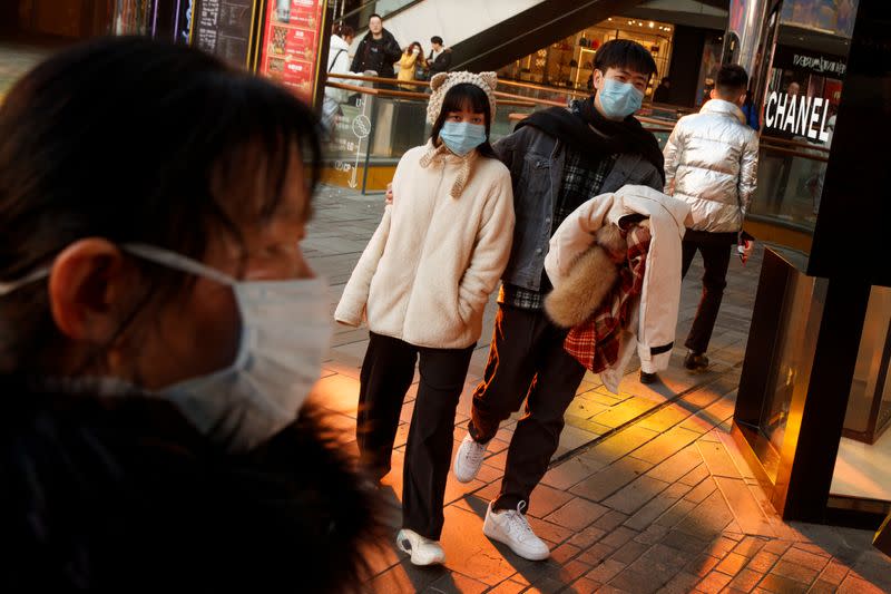 People wearing face masks walk past luxury boutiques in the Sanlitun shopping district in Beijing