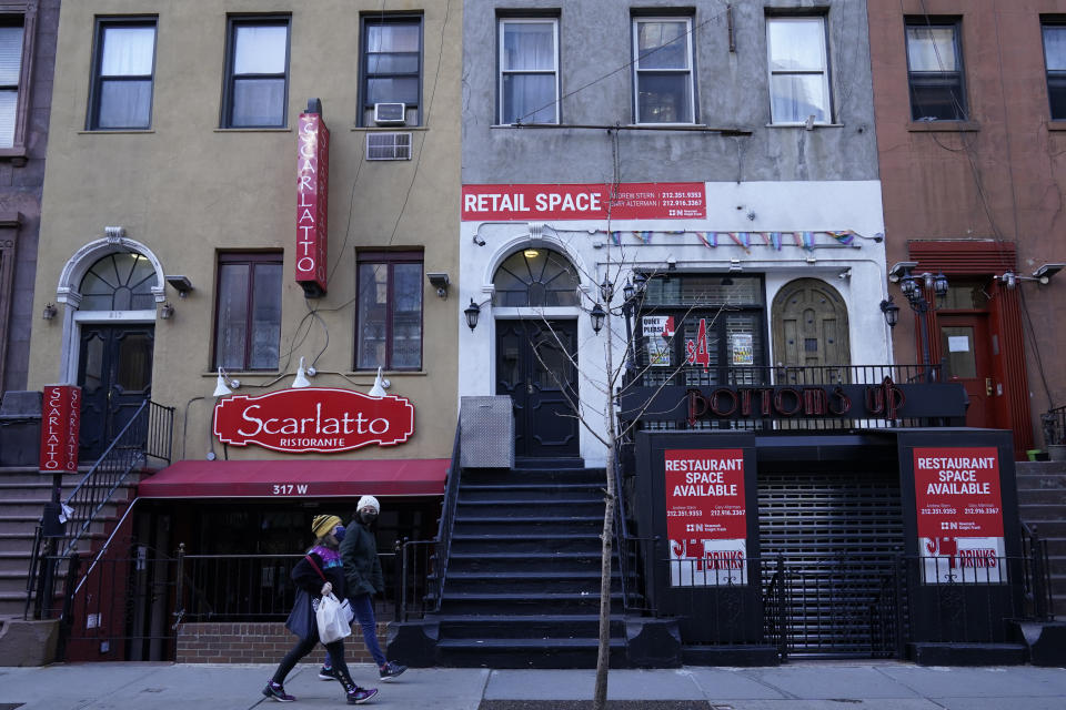 Pedestrians walk past a couple of closed restaurants on Restaurant Row, Sunday, Jan. 10, 2021, in the Hell's Kitchen neighborhood of New York. The boarded-up windows and For Rent signs are all over the place in Manhattan’s Hell’s Kitchen neighborhood. Nearby, the Broadway theaters are all dark. But the economic darkness brought on by the coronavirus pandemic has had a few bright spots. A couple of well-loved venues have gotten financial boosts, thanks to online fundraising campaigns and even a telethon. (AP Photo/Mary Altaffer)